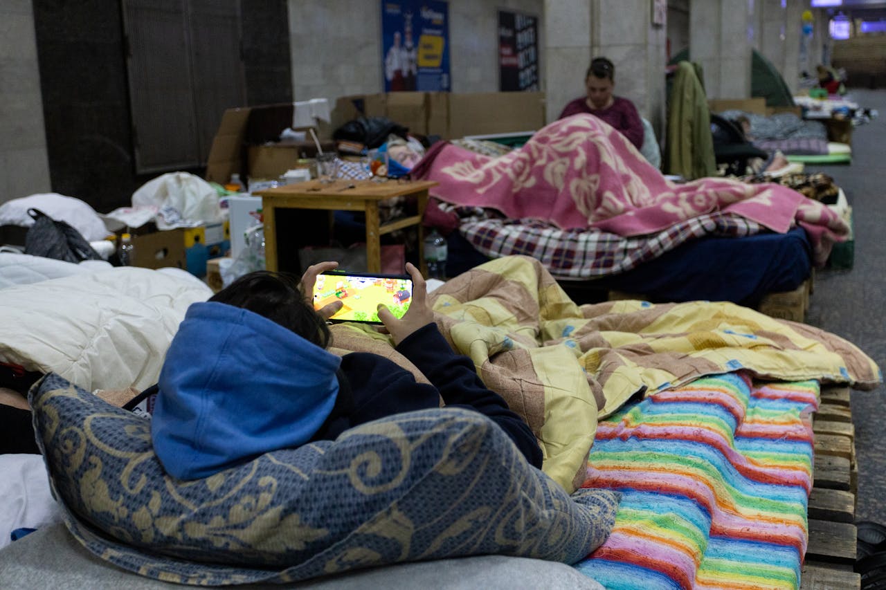 A busy evacuation center with people resting on makeshift beds and using mobile phones.